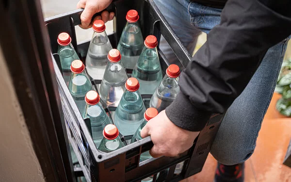 Eine nicht erkennbare Person hält eine Mehrwegkiste mit gefüllten Wasserflaschen in beiden Händen.