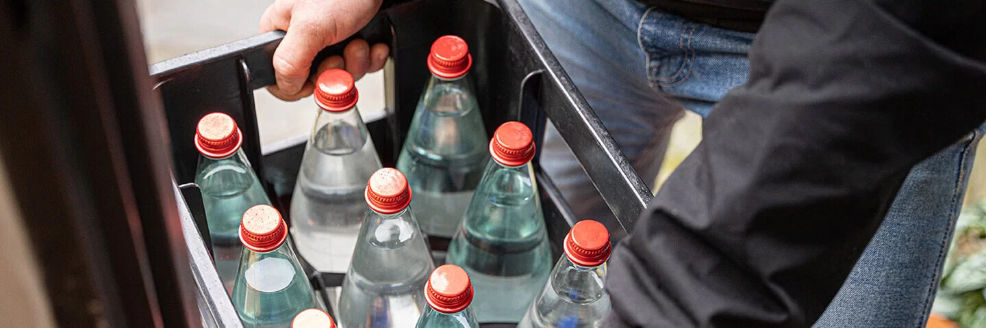 Eine nicht erkennbare Person hält eine Mehrwegkiste mit gefüllten Wasserflaschen in beiden Händen.