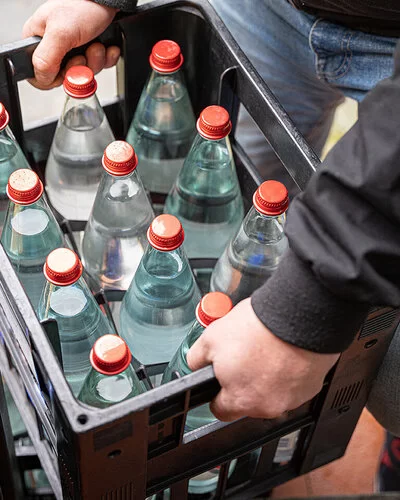 Eine nicht erkennbare Person hält eine Mehrwegkiste mit gefüllten Wasserflaschen in beiden Händen.