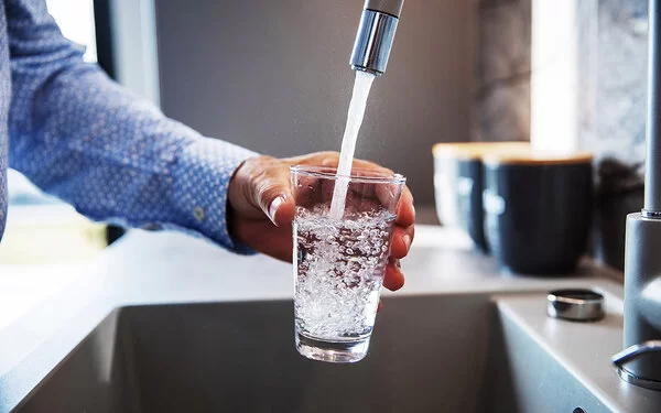 Ein Mann hält ein Glas unter den Wasserhahn und befüllt es mit Trinkwasser.