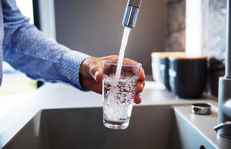 Ein Mann hält ein Glas unter den Wasserhahn und befüllt es mit Trinkwasser.