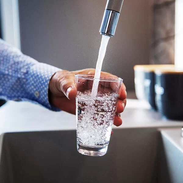 Ein Mann hält ein Glas unter den Wasserhahn und befüllt es mit Trinkwasser.