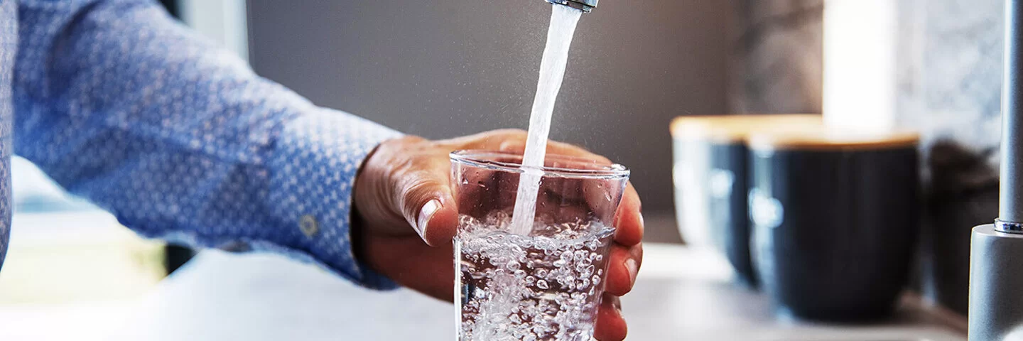 Ein Mann hält ein Glas unter den Wasserhahn und befüllt es mit Trinkwasser.