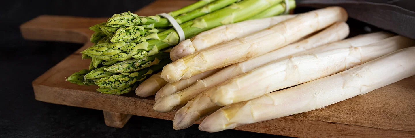 Grüner und weißer Spargel liegen auf einem Holzbrett.