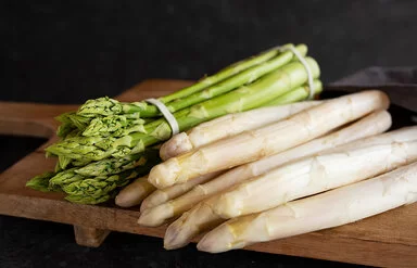 Grüner und weißer Spargel liegen auf einem Holzbrett.