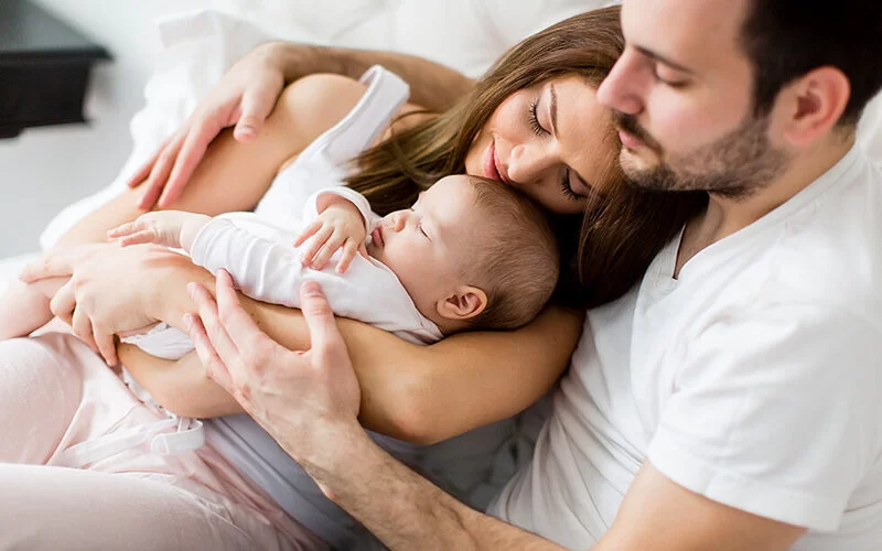 Eine Frau und ein Mann liegen sich innig in den Armen und kuscheln mit ihrem Baby.