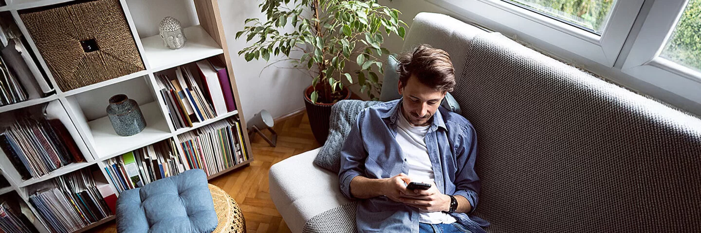 Ein Mann liegt auf einem Sofa und blickt auf sein Handy.