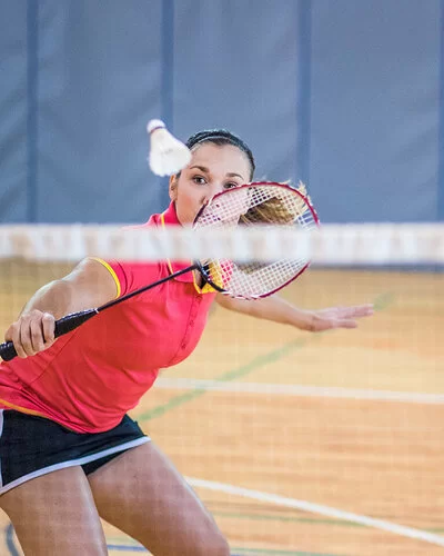 Eine Frau steht nah am Netz und schlägt einen Federball mit einem Badmintonschläger, während ihre Spielpartnerin, die hinter ihr steht, sie anschaut.