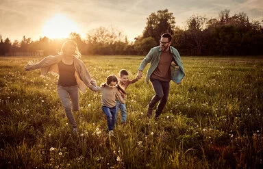 Familie springt freudig lachend übers Feld. 