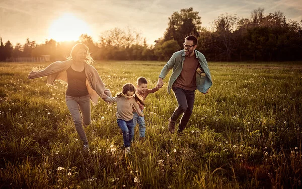 Familie springt freudig lachend übers Feld. 