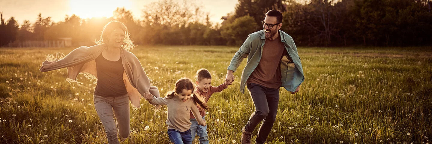 Familie springt freudig lachend übers Feld. 