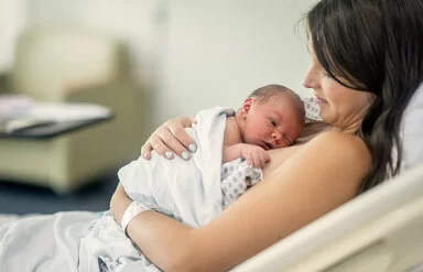 Eine Frau ruht in einem Bett und umarmt ihr neugeborenes Baby, das auf ihrer Brust liegt.