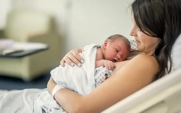 Eine Frau ruht in einem Bett und umarmt ihr neugeborenes Baby, das auf ihrer Brust liegt.