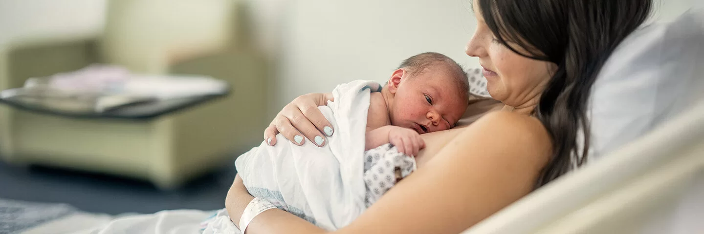 Eine Frau ruht in einem Bett und umarmt ihr neugeborenes Baby, das auf ihrer Brust liegt.