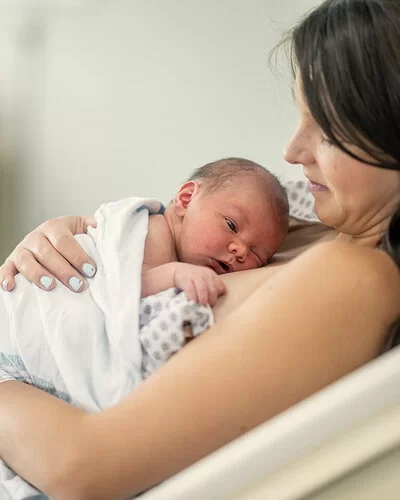 Eine Frau ruht in einem Bett und umarmt ihr neugeborenes Baby, das auf ihrer Brust liegt.