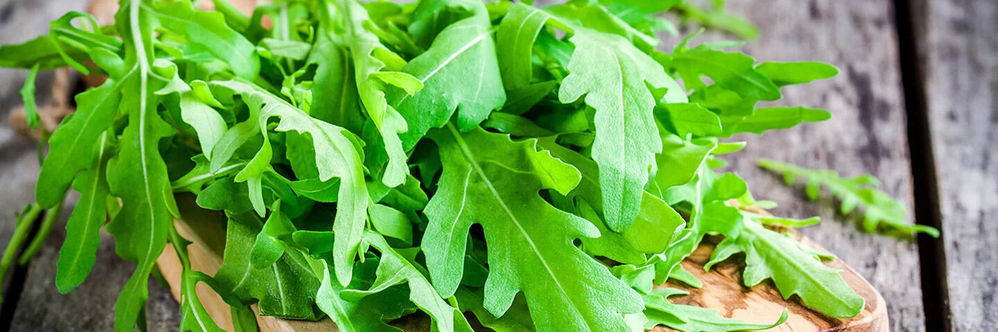 Frische Rucola-Blätter liegen auf einem Schneidebrett aus Holz.