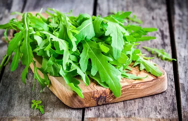 Frische Rucola-Blätter liegen auf einem Schneidebrett aus Holz.