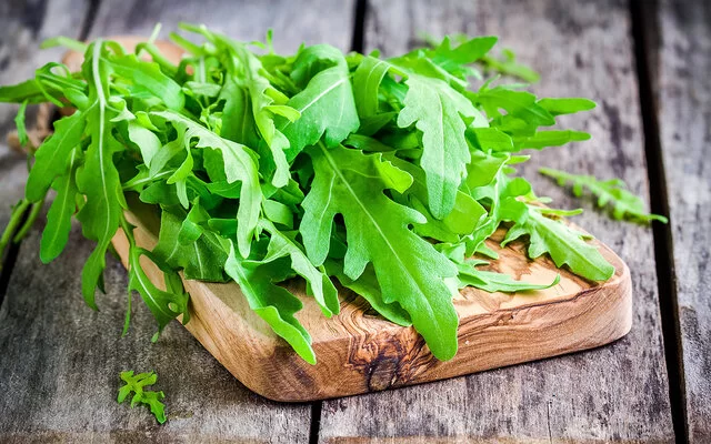 Frische Rucola-Blätter liegen auf einem Schneidebrett aus Holz.