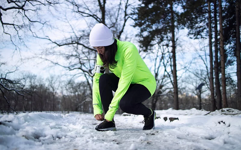 Joggerin in sportlicher Kleidung bindet sich im Winter die Schnürsenkel im Park.