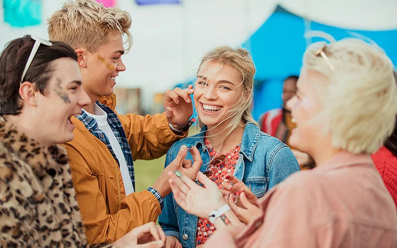 Eine Gruppe von Freunden, die sich bei einem Musikfestival gegenseitig Glitzer im Gesicht auftragen. 