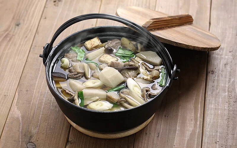 Japanische Pilzsuppe mit gemischten Pilzen und Lauchzwiebel in einem gusseisernen Topf.