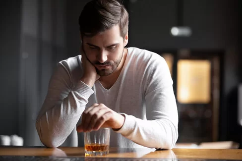 Junger Mann sitzt allein vor seinem Whiskey-Glas – ist das schon eine Sucht?
