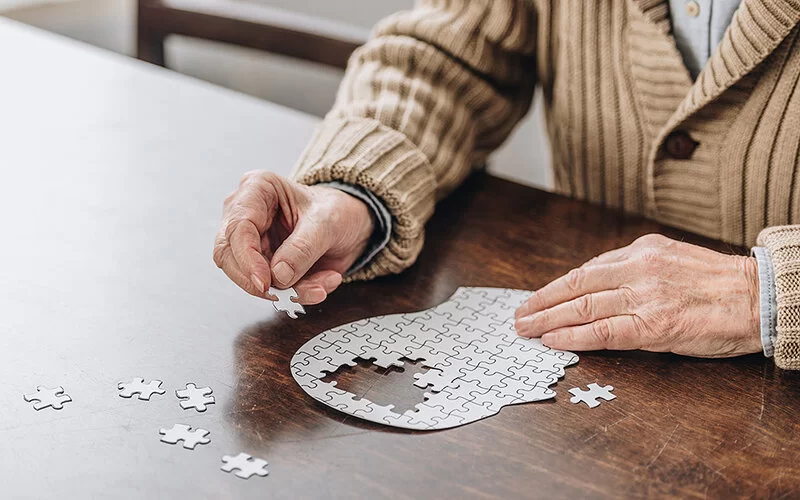 Eine Seniorin sitzt an einem Tisch und löst ein Puzzle.