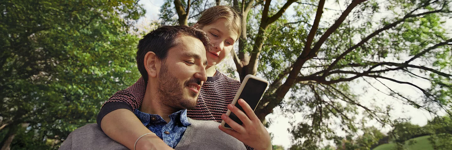 Eine Frau und ein Mann blicken auf ein Smartphone. Die Übertragung von Daten an die AOK erfolgt über eine Authentifizierung.