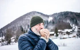 Ein Mann in Winterkleidung h�ält sich seine kalten Hände vor dem Mund, um sie zu wärmen.