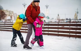 Ein Vater beim Schlittschuhlaufen mit seinen zwei kleinen Kindern.