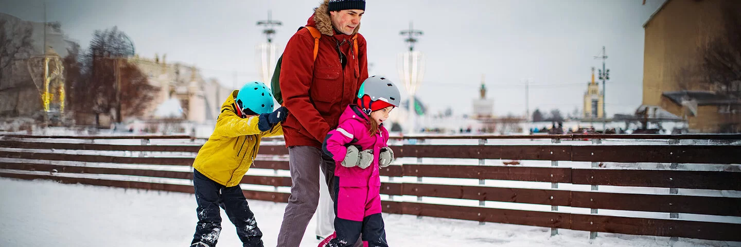 Ein Vater beim Schlittschuhlaufen mit seinen zwei kleinen Kindern.