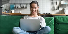 Junge Frau sitzt mit dem Laptop auf einem Sofa.