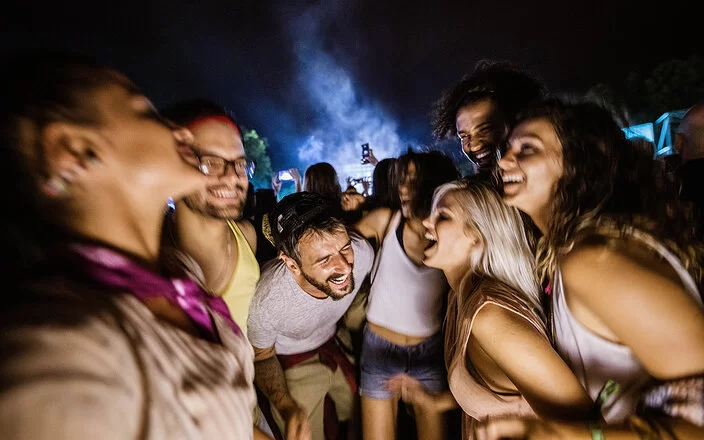 Eine Gruppe von sieben jungen Erwachsenen feiert euphorisch auf einer nächtlichen Outdoor-Party.