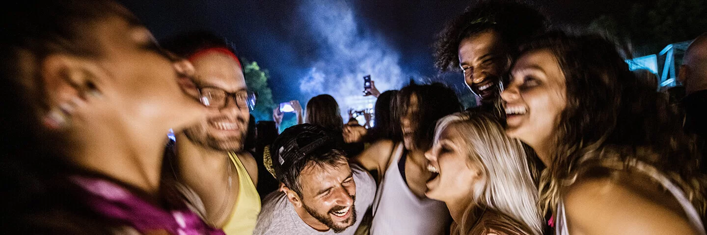 Eine Gruppe von sieben jungen Erwachsenen feiert euphorisch auf einer nächtlichen Outdoor-Party.