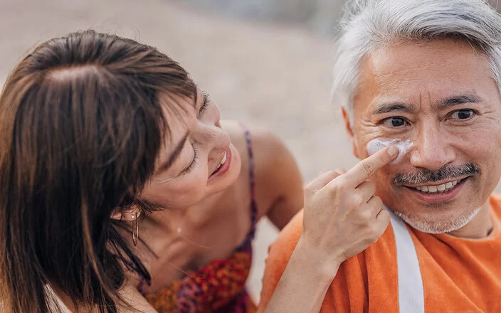 Eine Frau cremt einem Mann das Gesicht mit Sonnencreme ein.