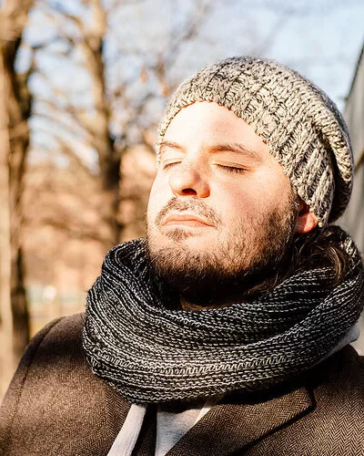 Ein Mann in herbstlicher Kleidung lehnt sich an einen Zaun, die Sonne scheint ihm ins Gesicht.