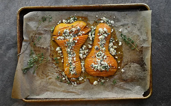 Hasselback Ofenkürbis mit Feta und Thymian auf einem mit Backpapier ausgelegten Backblech.