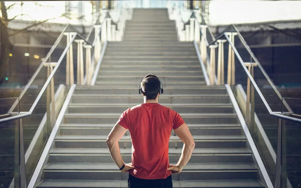 Ein Mann mit einem roten T-Shirt und Kopfhörern steht vor einer Treppe und blickt die Stufen herauf.