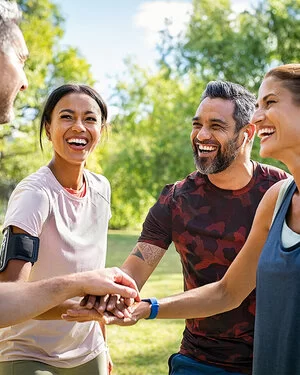 Zwei Männer und zwei Frauen stehen im Park lächelnd beisammen und legen die Hände übereinander. Die AOK-SportTreffs in Baden-Württemberg sind sehr beliebt.