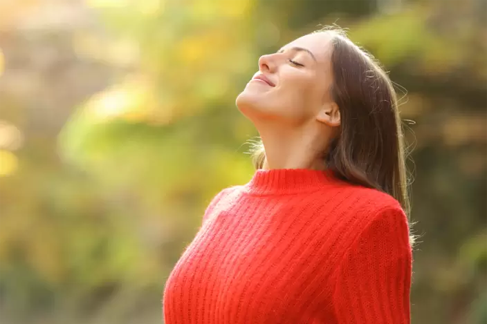 Eine junge Frau steht in der Natur und atmet durch.