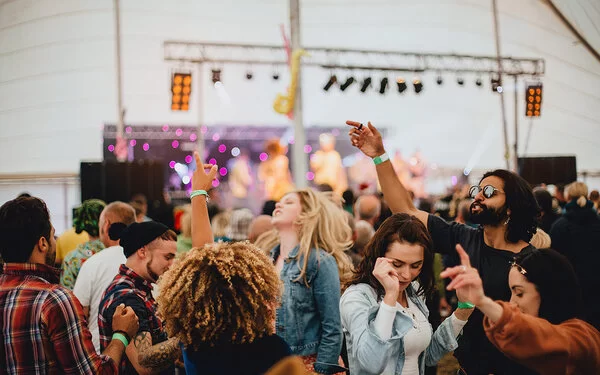Festival-Spaß – Nahaufnahme einer Gruppe Menschen, die ausgelassen vor einer Bühne in einem Festzelt tanzt.
