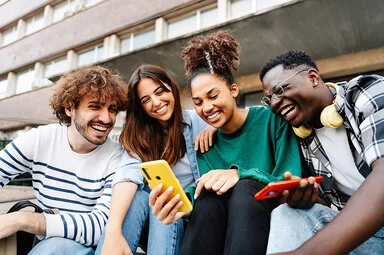 Mehrere Studenten auf dem Campus sitzen entspannt beieinander und lachen miteinander.