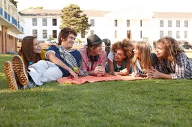 Mehrere Studenten auf dem Campus liegen entspannt beieinander und lachen miteinander.