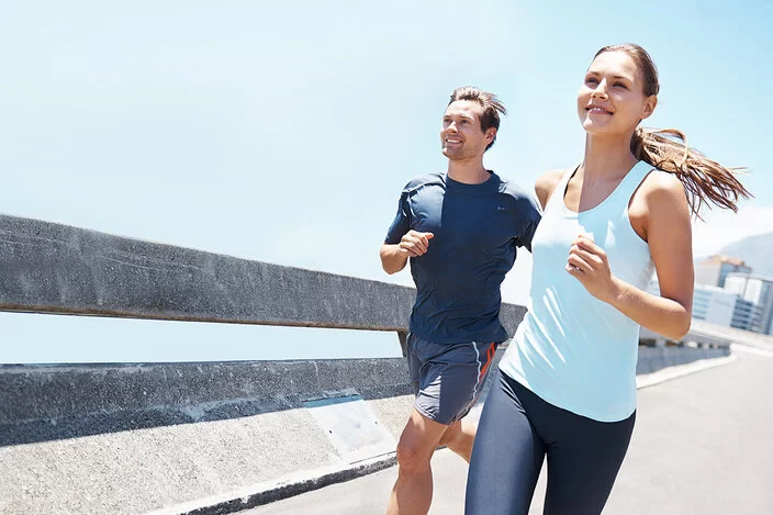 Eine Frau und ein Mann joggen in Sportkleidung an einem sonnigen Tag. 