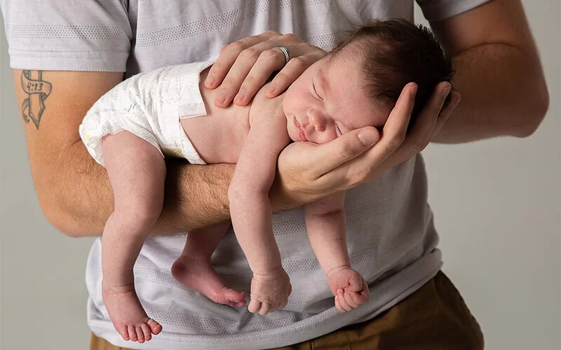 Ein Baby ruht im Fliegergriff auf dem Unterarm eines Mannes.