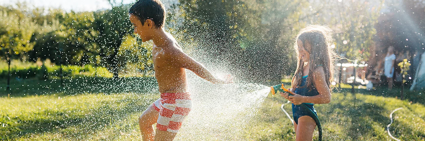 Ein Junge und ein Mädchen kühlen sich an einem heißen Sommertag im Garten mit Wasser aus einem Gartenschlauch ab.