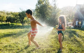 Ein Junge und ein Mädchen kühlen sich an einem heißen Sommertag im Garten mit Wasser aus einem Gartenschlauch ab.