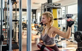 Eine junge Frau trainiert im Fitnessstudio an einem Latzug-Gerät.