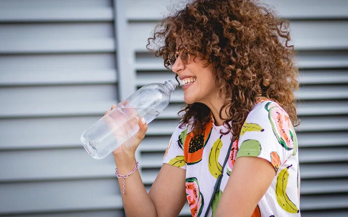 Junge Frau trinkt klares Glas Wasser.