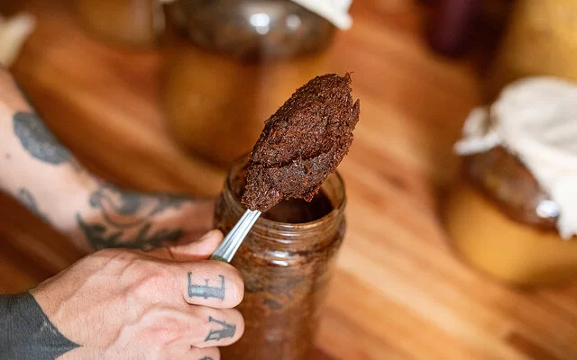Eine Person entnimmt mit einem Löffel Miso-Paste aus einem Glas.